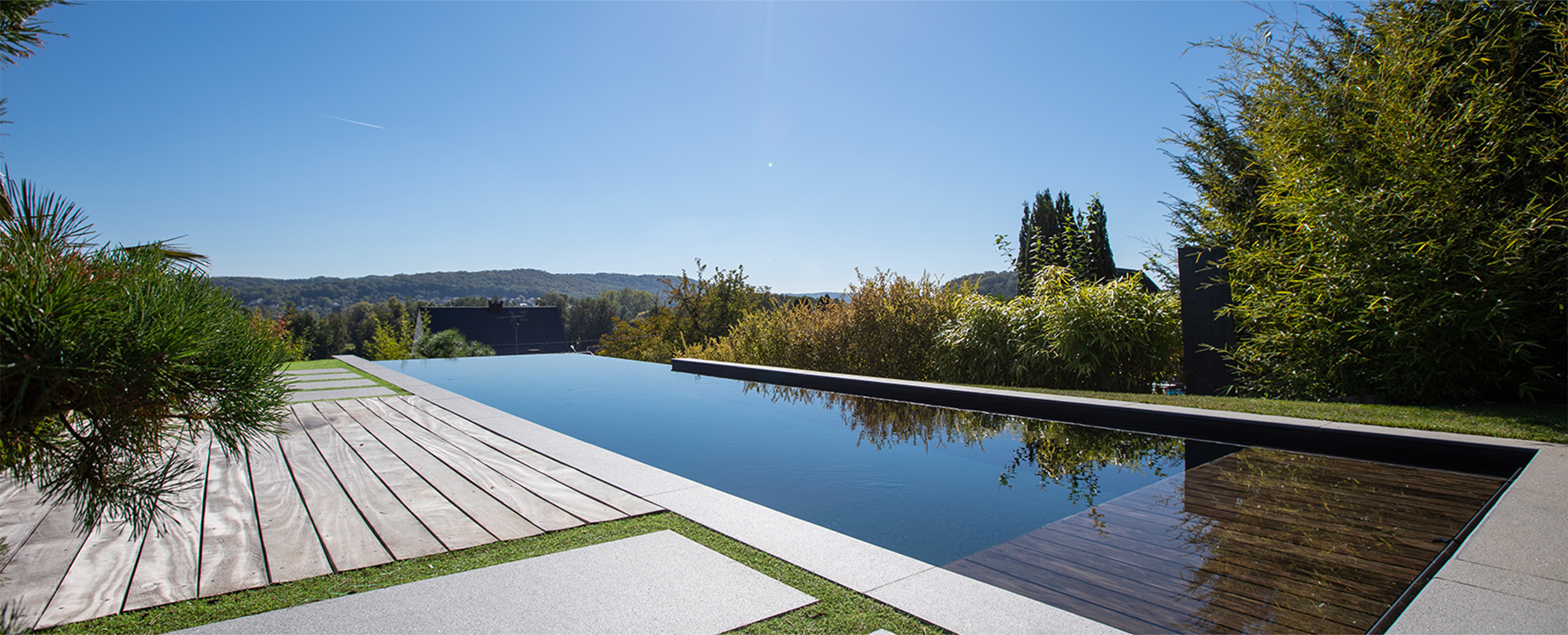 Piscine miroir et terrasse bois – Pool68 Piscine miroir rectangulaire avec terrasse bois et vue sur la vallée, réalisation Pool68